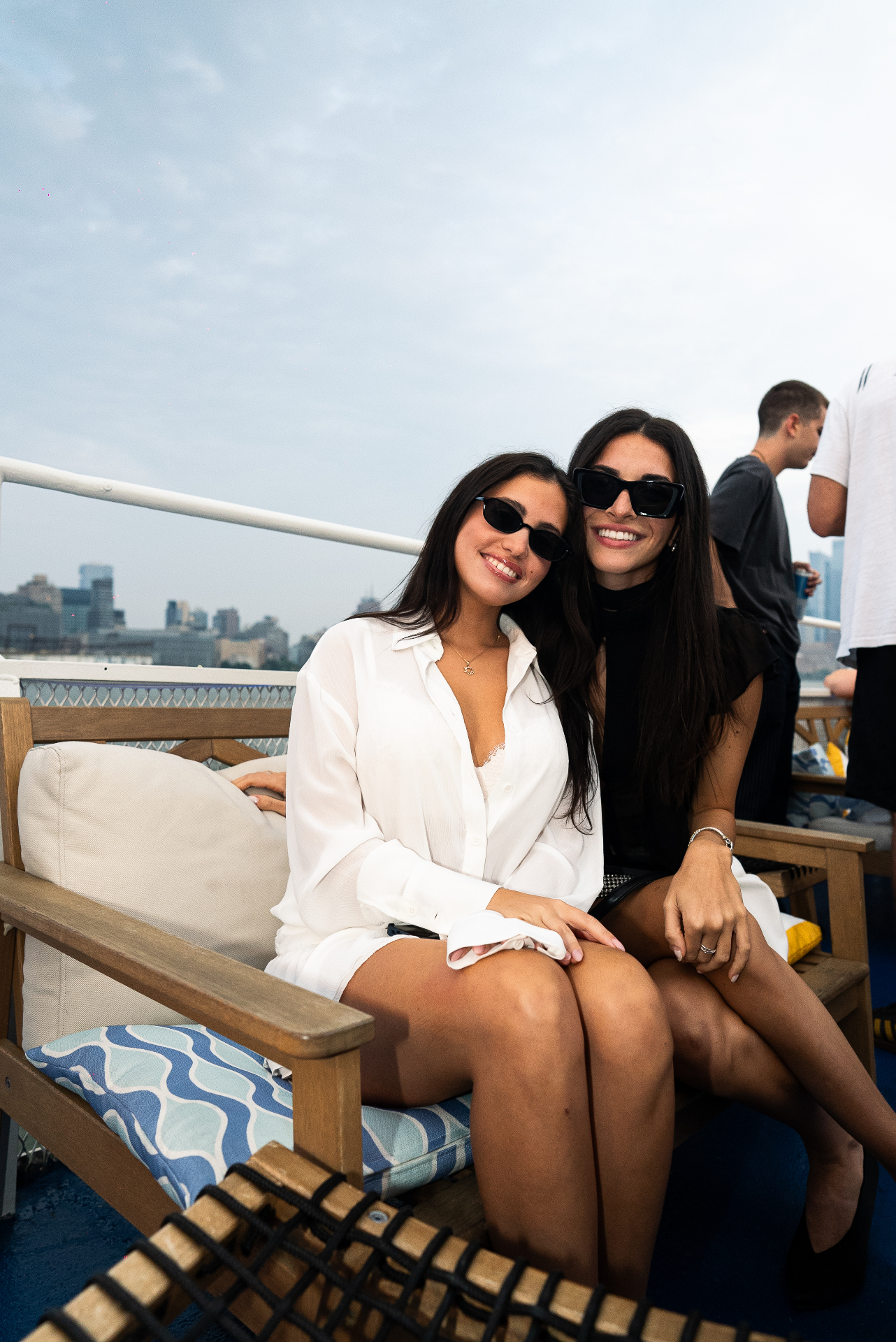 Two friends smiling on a private yacht event with the Manhattan skyline behind